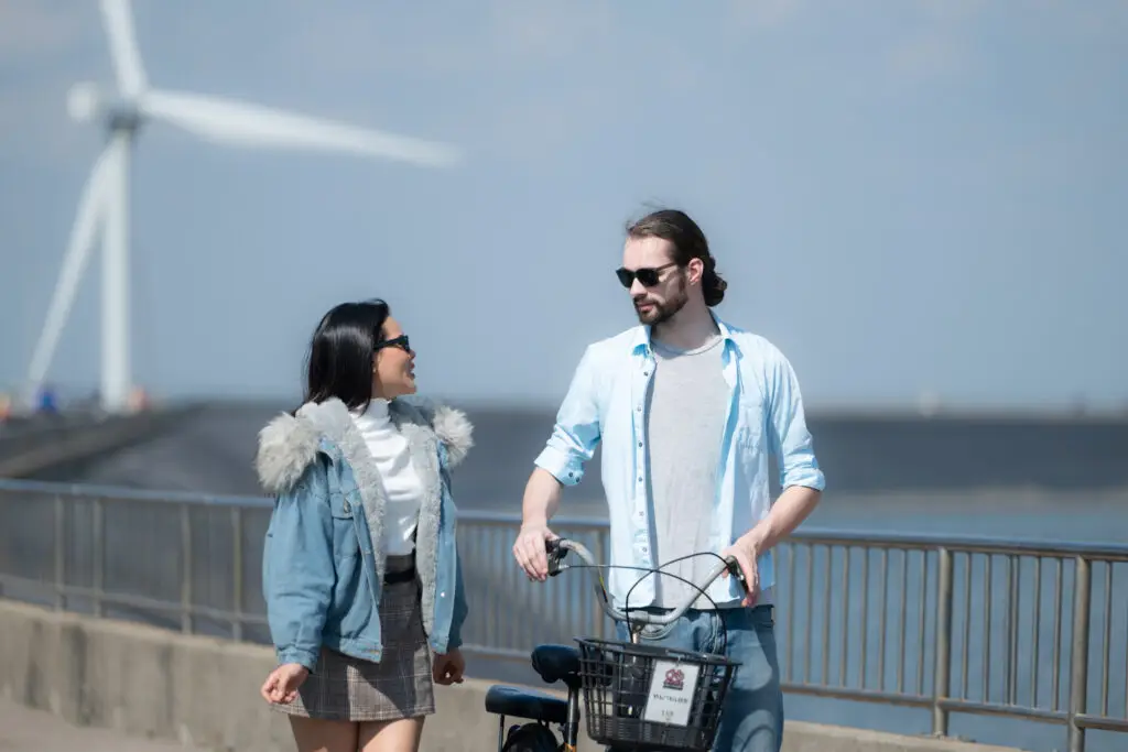 Young couple relaxing by a wind turbine in the Netherlands during a film production shoot